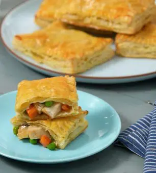 Image of chicken pot pie pockets on plates with one cut open showing meat, veggies and gravy inside