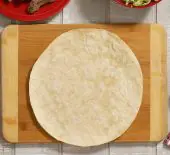A tortilla on a cutting board ready to start assembling a Steak Fajita Crunchwrap