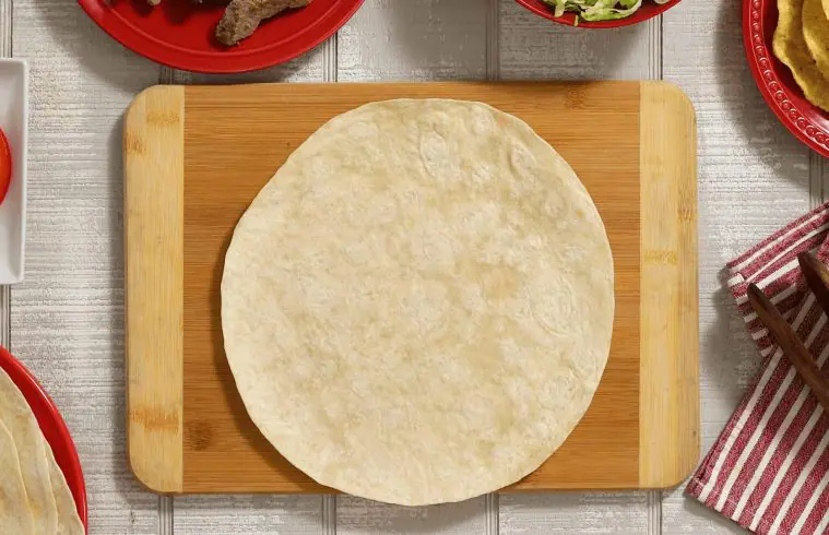 A tortilla on a cutting board ready to start assembling a Steak Fajita Crunchwrap
