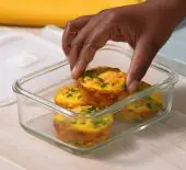 Image of finished Make Ahead Egg Bites in a glass storage container with a person grabbing one to eat