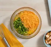 image of a glass mixing bowl filled with cheese, bell pepper, parsley and eggs