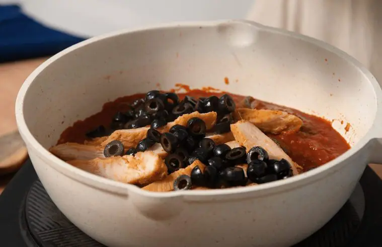 An image showing olives and John Soules Foods Seasoned Rotisserie Chicken in a pot of tomato sauce to make Chicken Cacciatore.