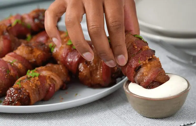 A person's hand dipping a Sweet and Spicy Bacon Wrapped BBQ Chicken Strip into ranch